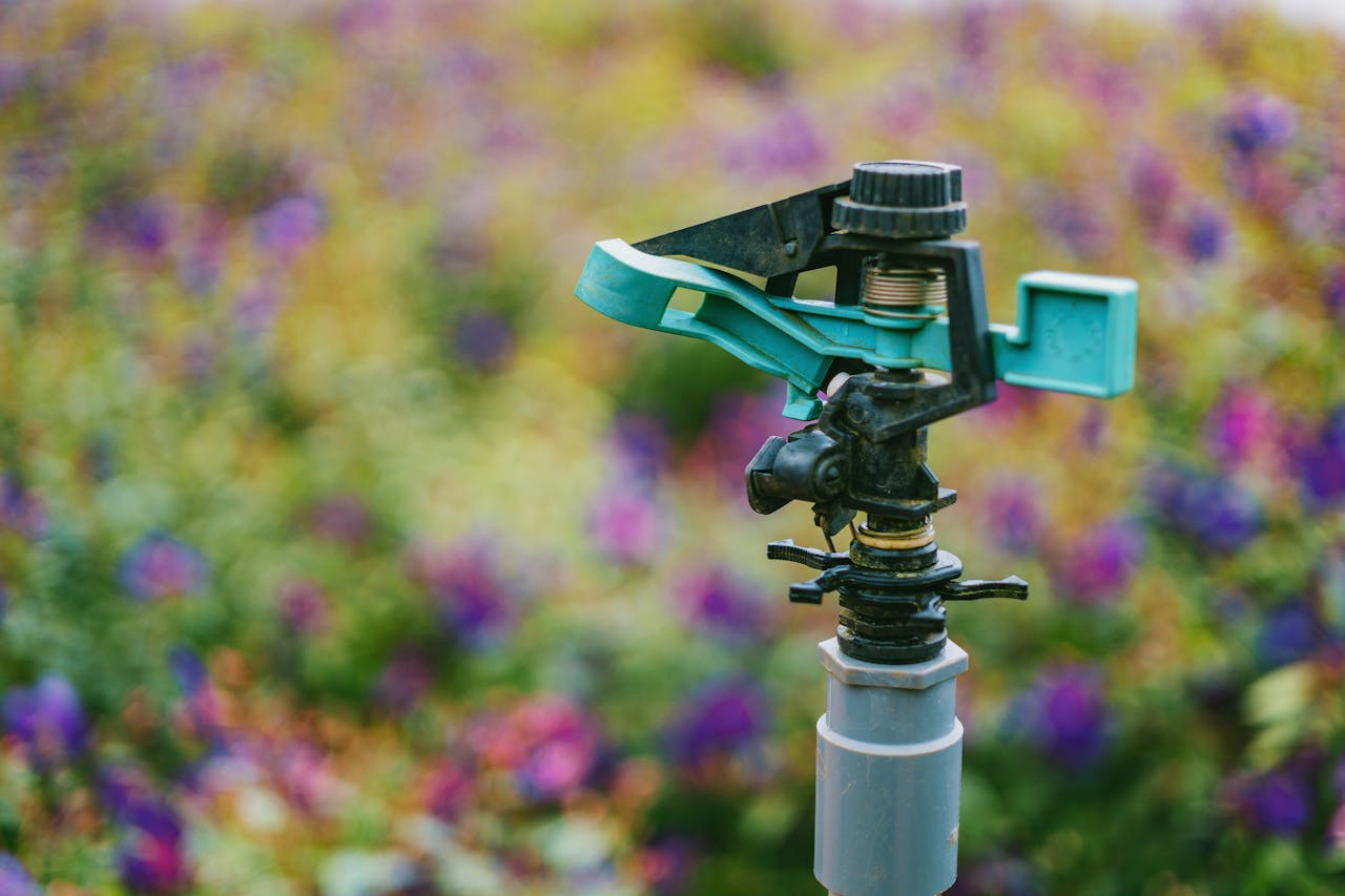 gallery-01 Detailed close-up of a garden sprinkler with colorful flowers in soft focus background.